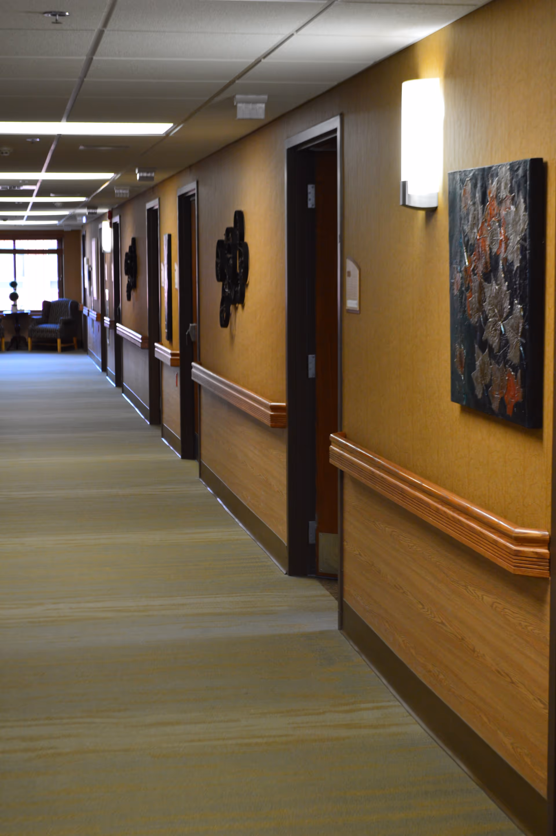 Carpeted interior hallway with doors, wooden handrails, wall art and a seating area at the far end.