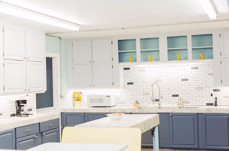 Bright modern kitchen with white subway-tile backsplash, blue lower cabinets, white upper cabinets, an island, and a microwave.