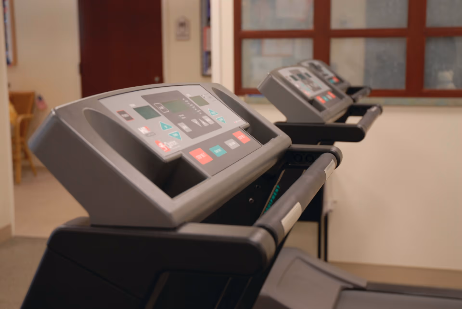 Close-up view of two treadmills in a fitness room with a window and a door in the background.