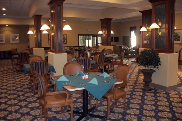 Indoor dining room in a senior living facility with teal tablecloths and lamps.