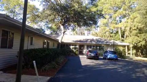 Exterior view of a single-story senior living facility with parking and trees.