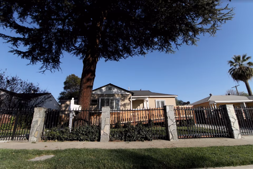 Single-story beige senior living building behind a black iron fence and large tree.