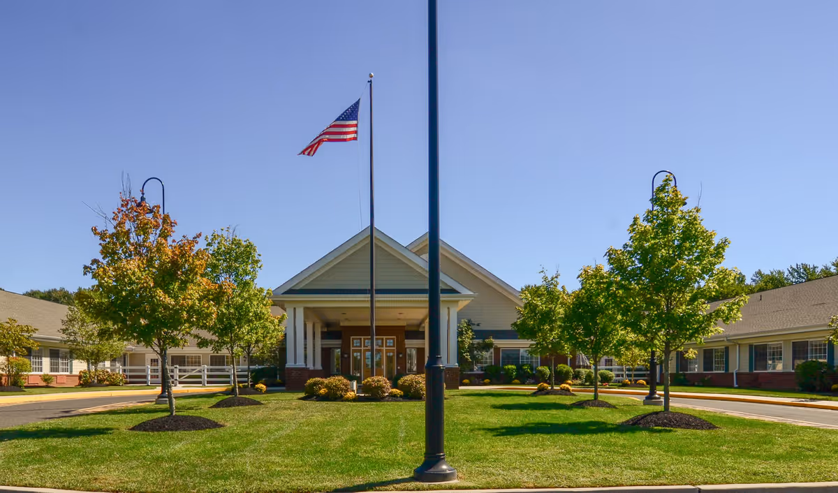 Front exterior view of Atlas Healthcare Washington Township building with a neatly manicured lawn, several trees, an American flag on a flagpole, and a clear blue sky.