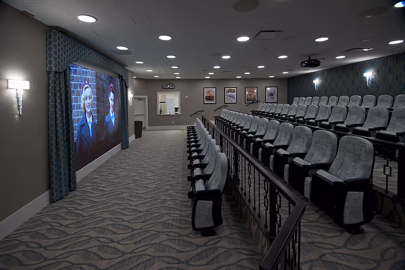 Tiered private movie theater with upholstered seats facing a large projection screen in a senior living facility.