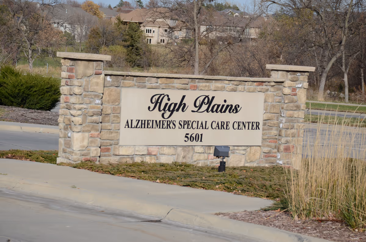 Stone sign at the entrance of High Plains Alzheimer's Special Care Center with the address number 5601, surrounded by landscaping and trees in the background.