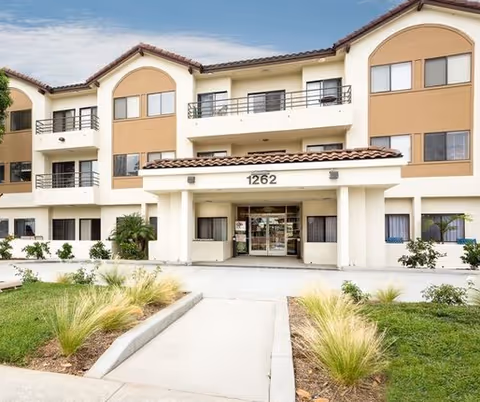 Three-story beige senior living building with arched windows and a central entrance.