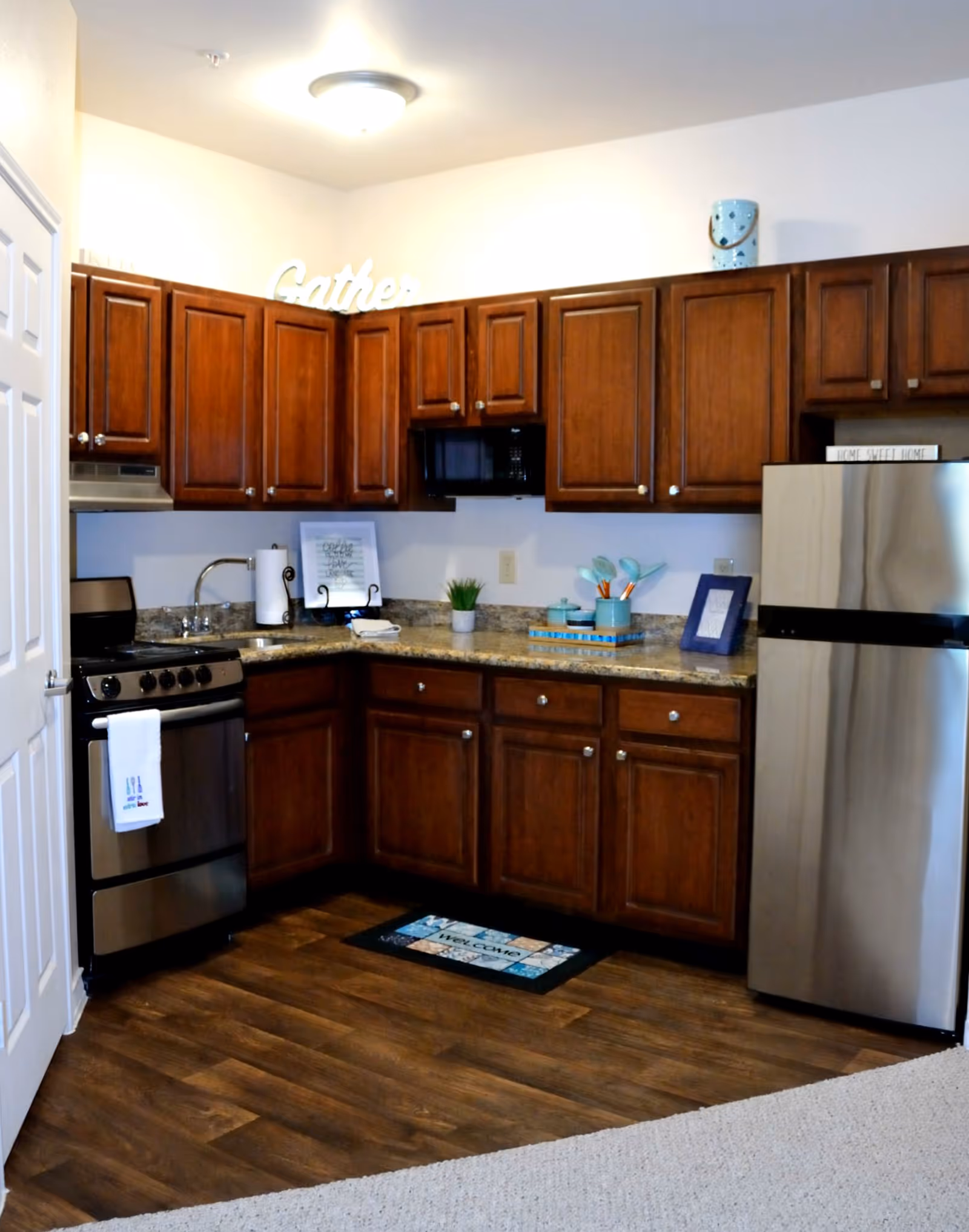 Small kitchen with wooden cabinets, stainless steel stove and refrigerator, granite countertops, and hardwood floor.