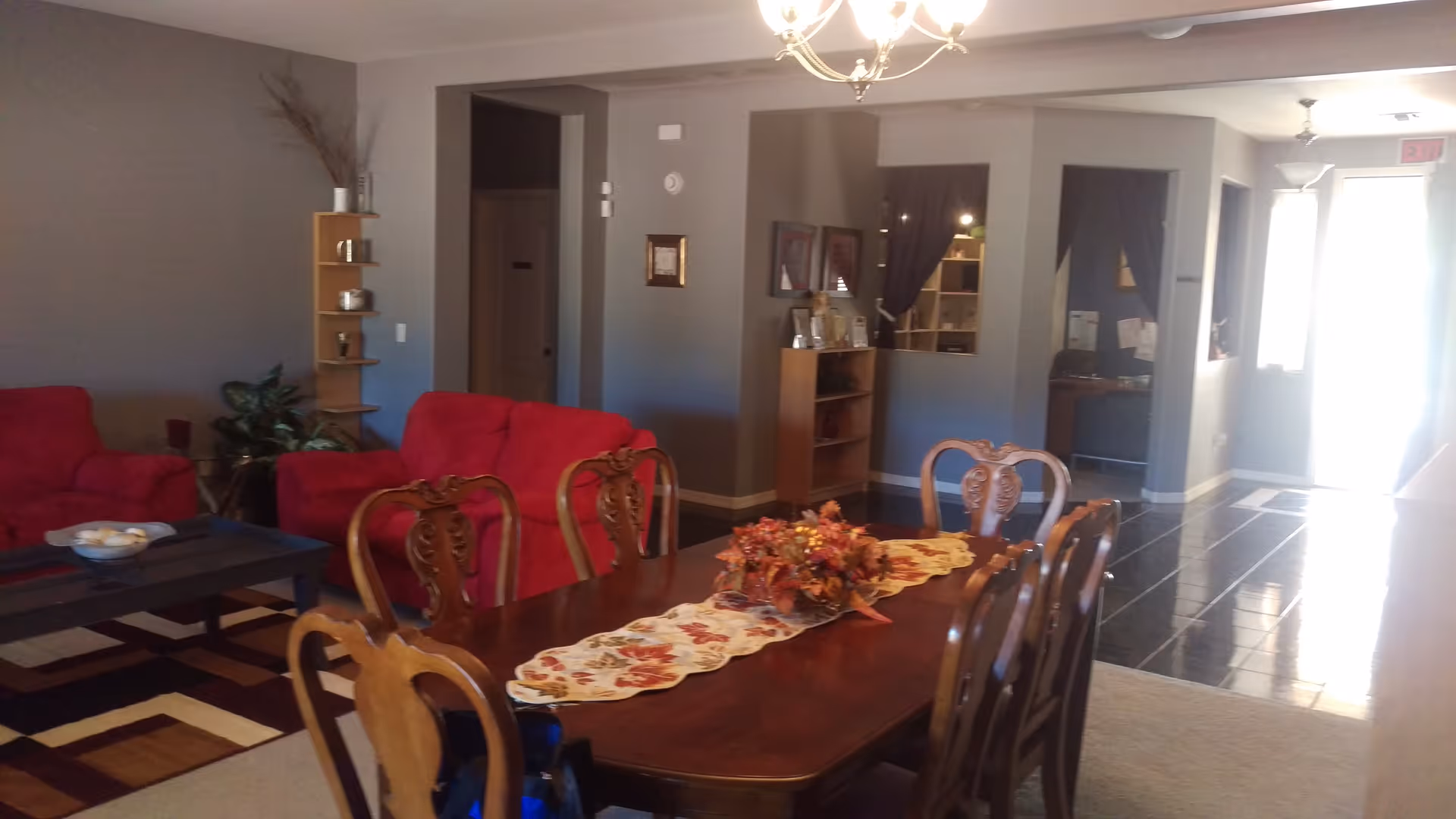 Open dining and living room with a wooden dining table and chairs, a floral centerpiece, red sofas and a coffee table.