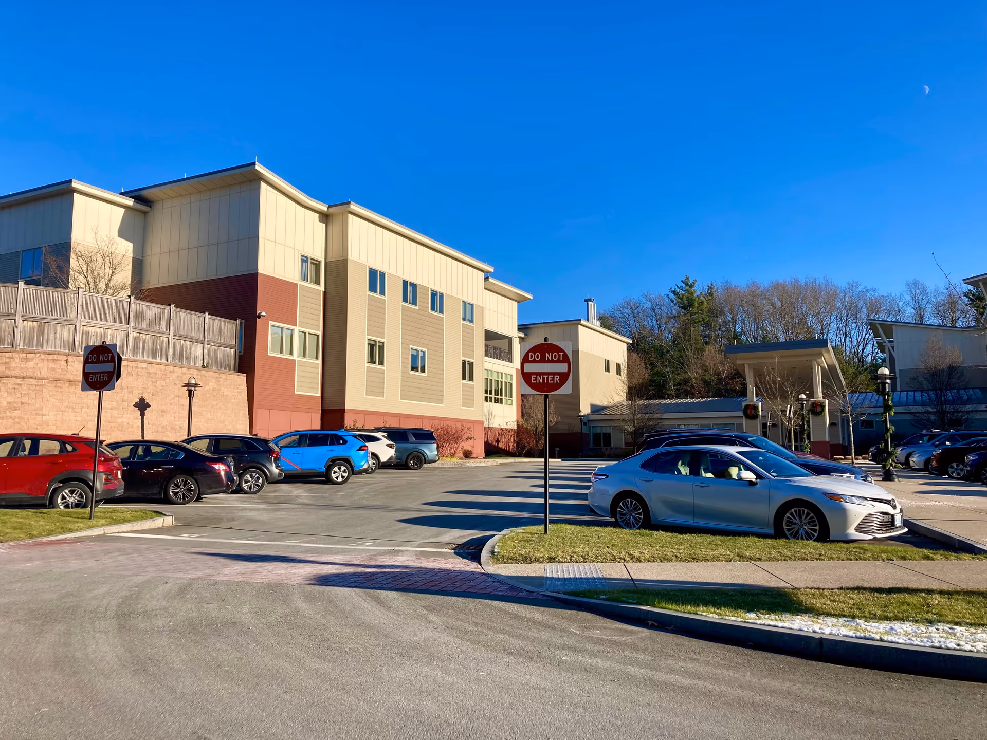 Parking lot outside a multi-story building at North Hill Retirement Community with several parked cars, clear blue sky, and two 'Do Not Enter' signs visible.