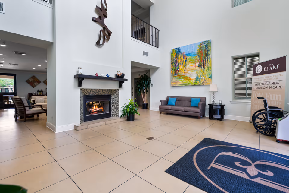 Spacious senior living lobby with a fireplace, seating area, colorful wall art, and a welcome rug.
