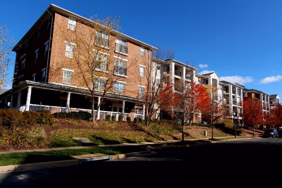 Front view of a multi-story brick residential building with porches, balconies and trees with autumn foliage under a clear blue sky.