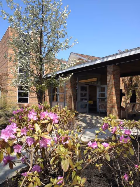 Brick senior living facility entrance with glass doors and blooming foreground flowers.