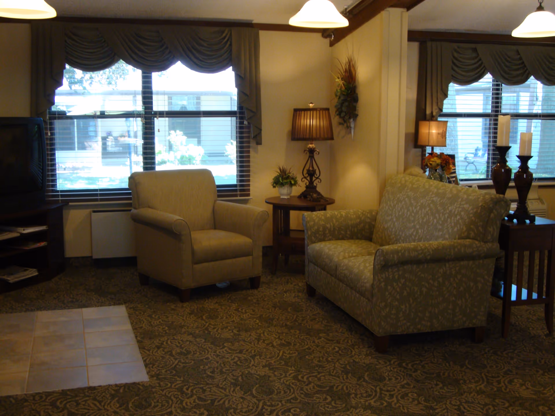 Comfortable sitting area in a lounge with armchairs, side tables, lamps, and large windows.
