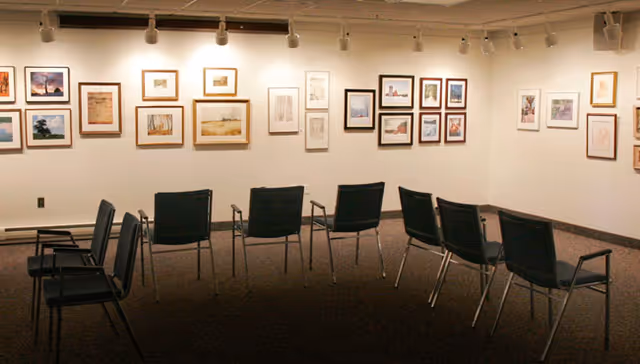 A small gallery-style common room with rows of chairs facing a wall hung with framed artwork.