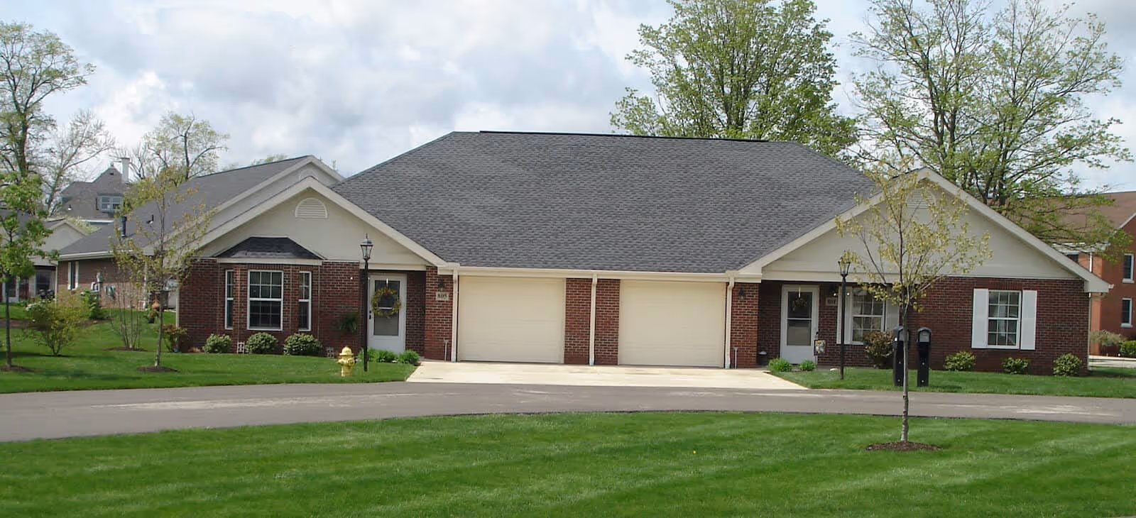 Front view of a single-story brick duplex with two garage doors, front porches, and a well-kept lawn.