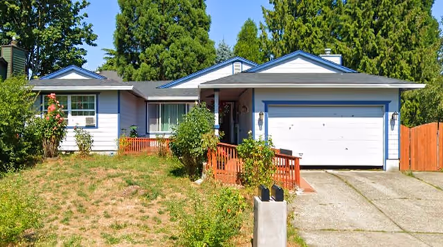 Single-story ranch-style house with an attached two-car garage, front porch and ramp, and a grassy front yard with shrubs.