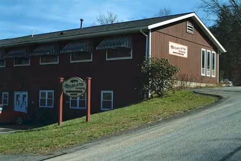 Brown Highland Oaks building with road, sign, and grassy slope outside.