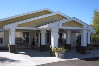 Front entrance of a single-story building with a covered porte-cochere supported by white columns and planters.