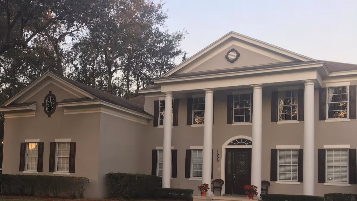 Front exterior of a two-story colonial-style house with large white columns, shuttered windows, and a central entrance.