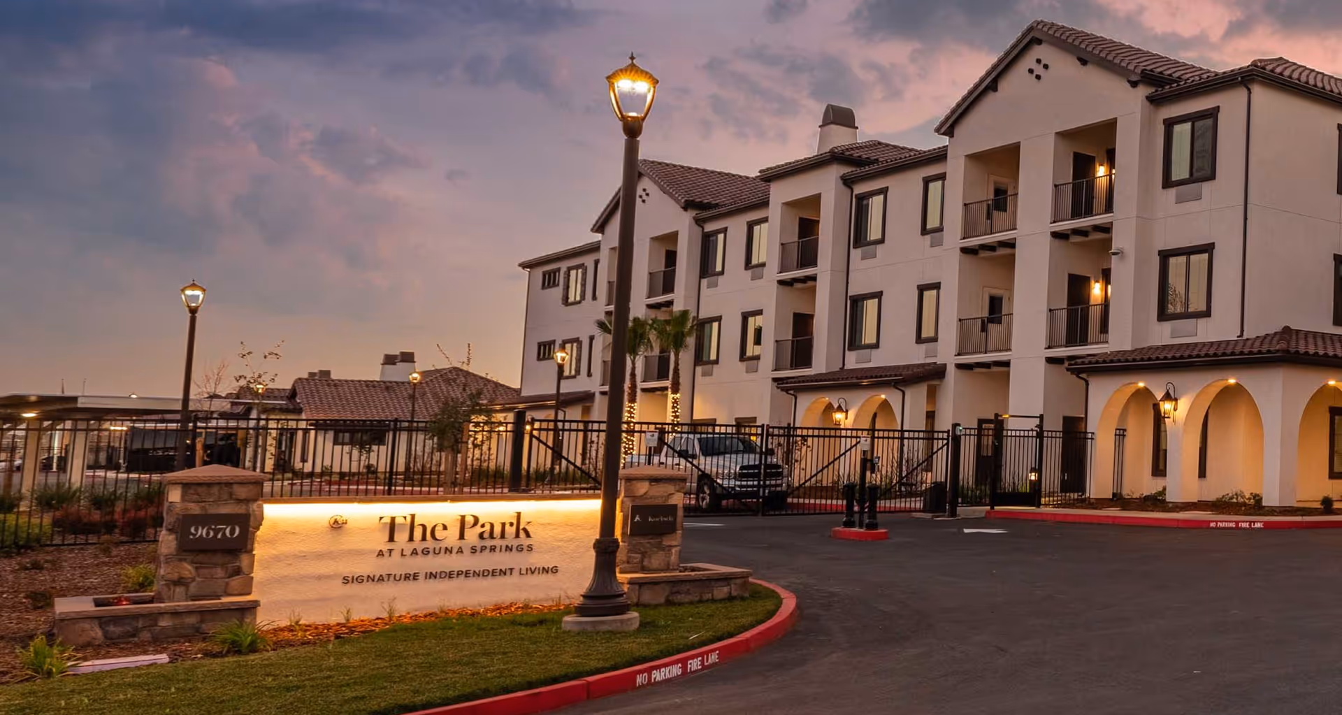 Exterior front entrance of The Park at Laguna Springs senior living building with illuminated sign at dusk.