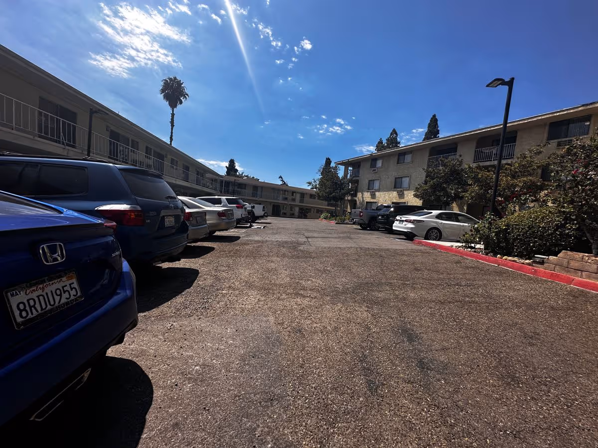 Parking lot with several cars parked in front of a two-story senior living building under a sunny blue sky.