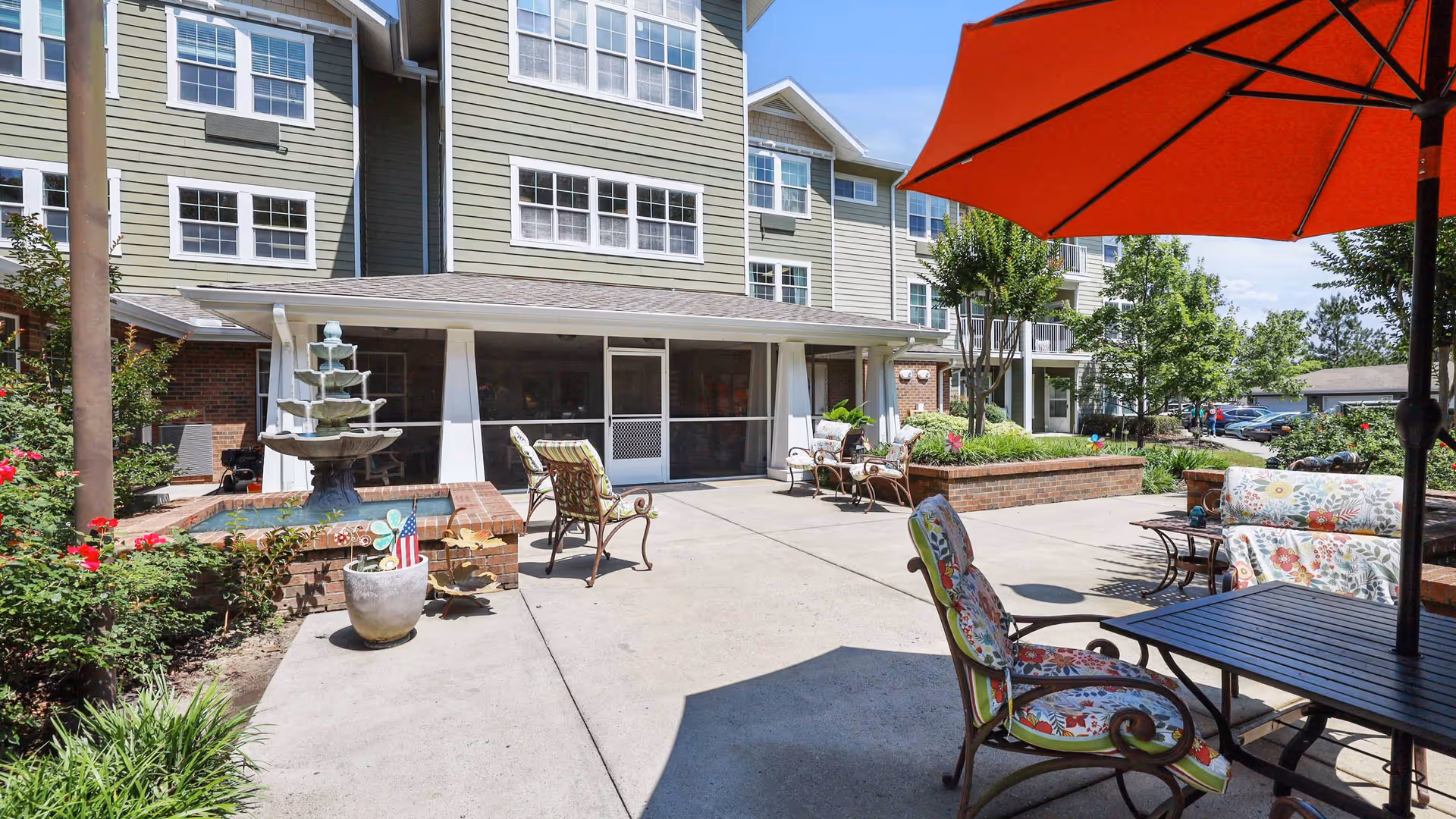 Sunny outdoor courtyard with patio seating, a multi-tiered fountain, and the building façade in the background.