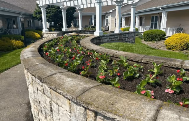 Curved stone planter with blooming flowers surrounds a courtyard beside senior living buildings
