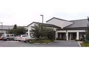 Exterior view of Enterprise Health & Rehabilitation Center showing a single-story building with a covered entrance, several parked cars, and landscaped greenery including trees and bushes.