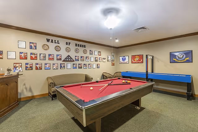 Recreation room with a red pool table, shuffleboard, seating and a 'Wall of Honor' display on the wall.