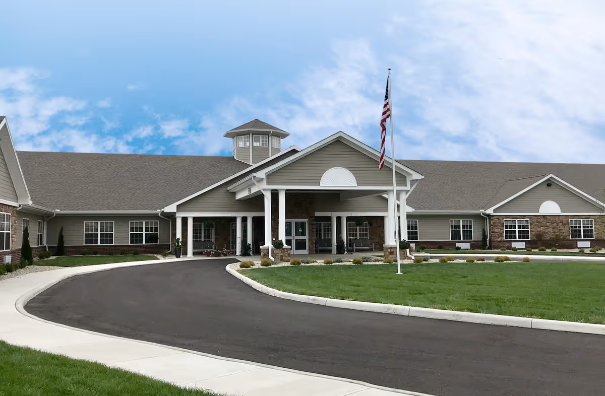 Front entrance of a single-story senior living facility with a covered portico, American flag, and circular driveway.