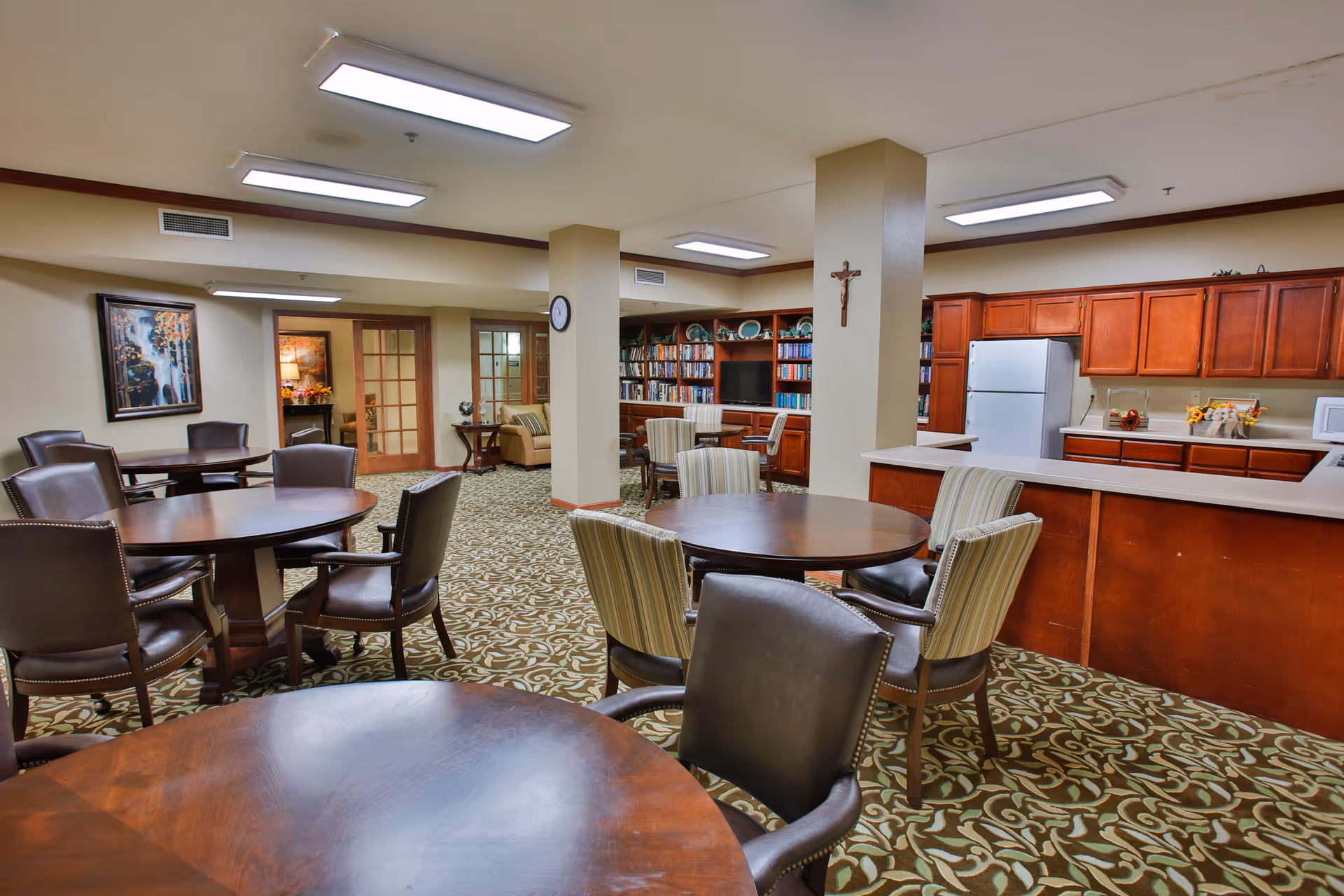 Community common room with round tables and chairs, a kitchenette and bookshelves.