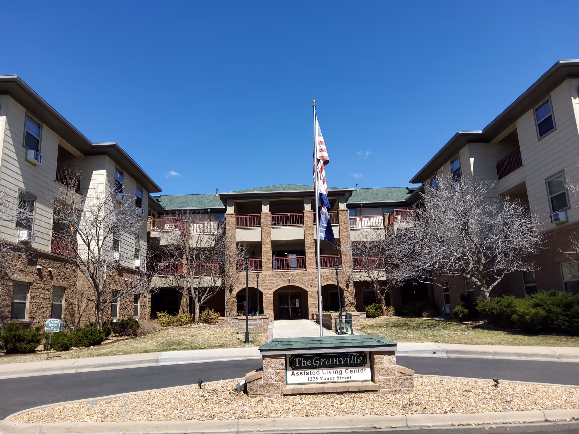 Front exterior of The Granville Assisted Living Center with its entrance, central flagpole, and sign in the foreground.