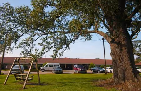 Exterior view of Twin Oaks Nursing and Convalescent Home with cars and trees.