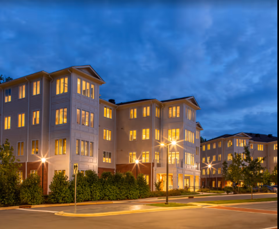 Multi-story residential building exterior illuminated at dusk with many lit windows and streetlights.