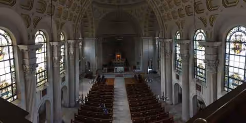 Inside a grand chapel with pews, stained-glass windows, and an altar.