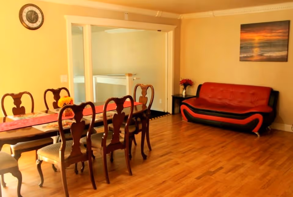 Dining room with a wooden table and six chairs, hardwood floor, and a red-and-black sofa against the wall.