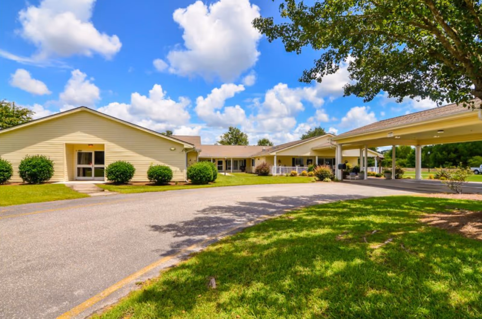 Exterior view of a single-story senior living center with driveway, entrance, and well-kept lawn.