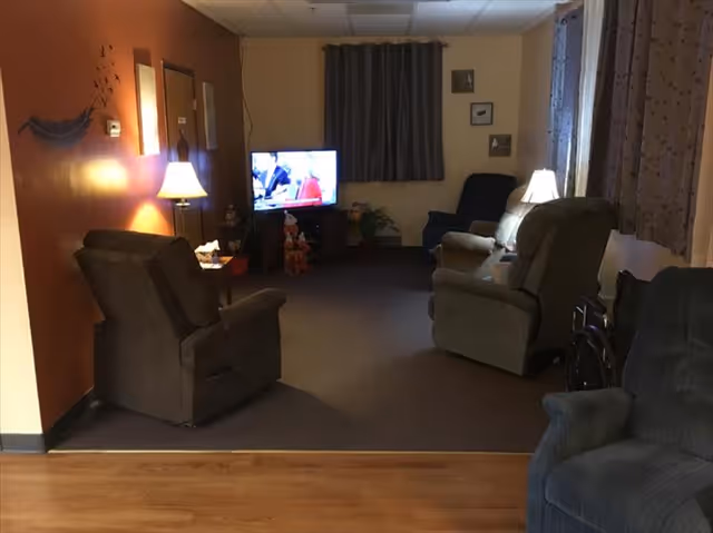 Cozy living room with several recliner chairs arranged around a TV, side lamps, and curtained windows.