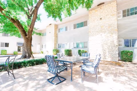 Outdoor patio with a glass table and striped chairs under a large tree.