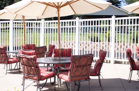 Outdoor patio with round tables, red cushioned chairs and large umbrellas beside a white fence.