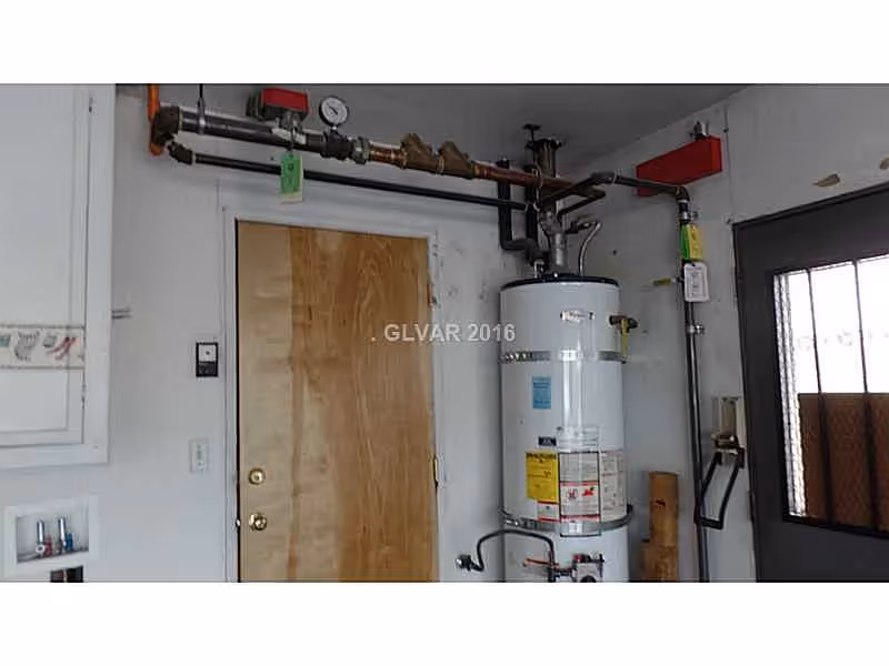 A utility room with a water heater, exposed piping, a wooden interior door, and a metal side door.