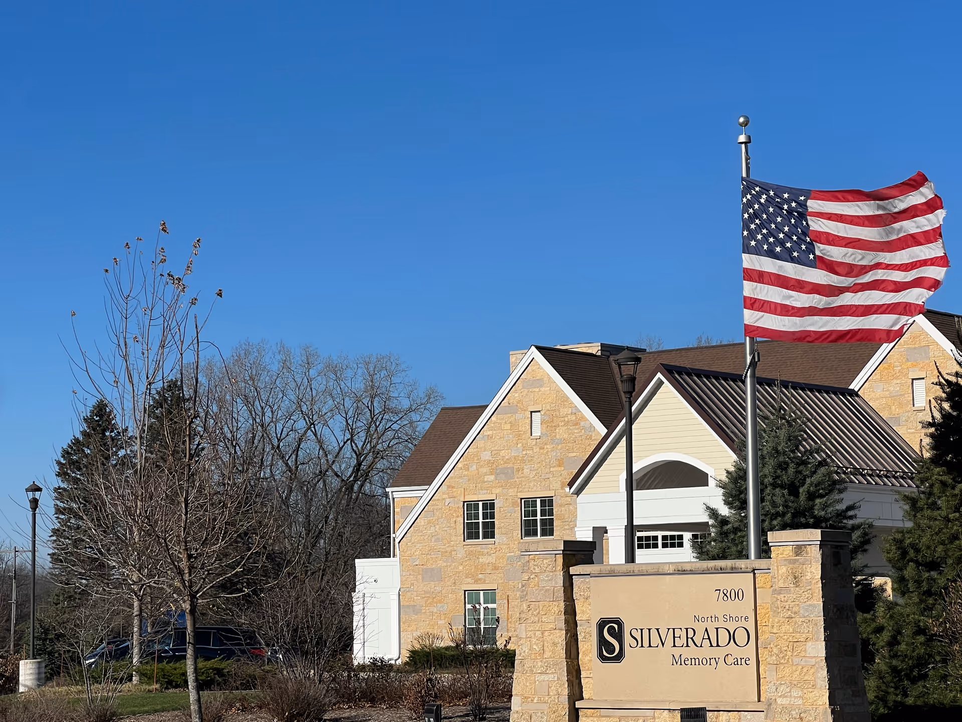 Entrance of the Silverado North Shore Memory Care building with a stone facade, facility sign, and an American flag on a pole.