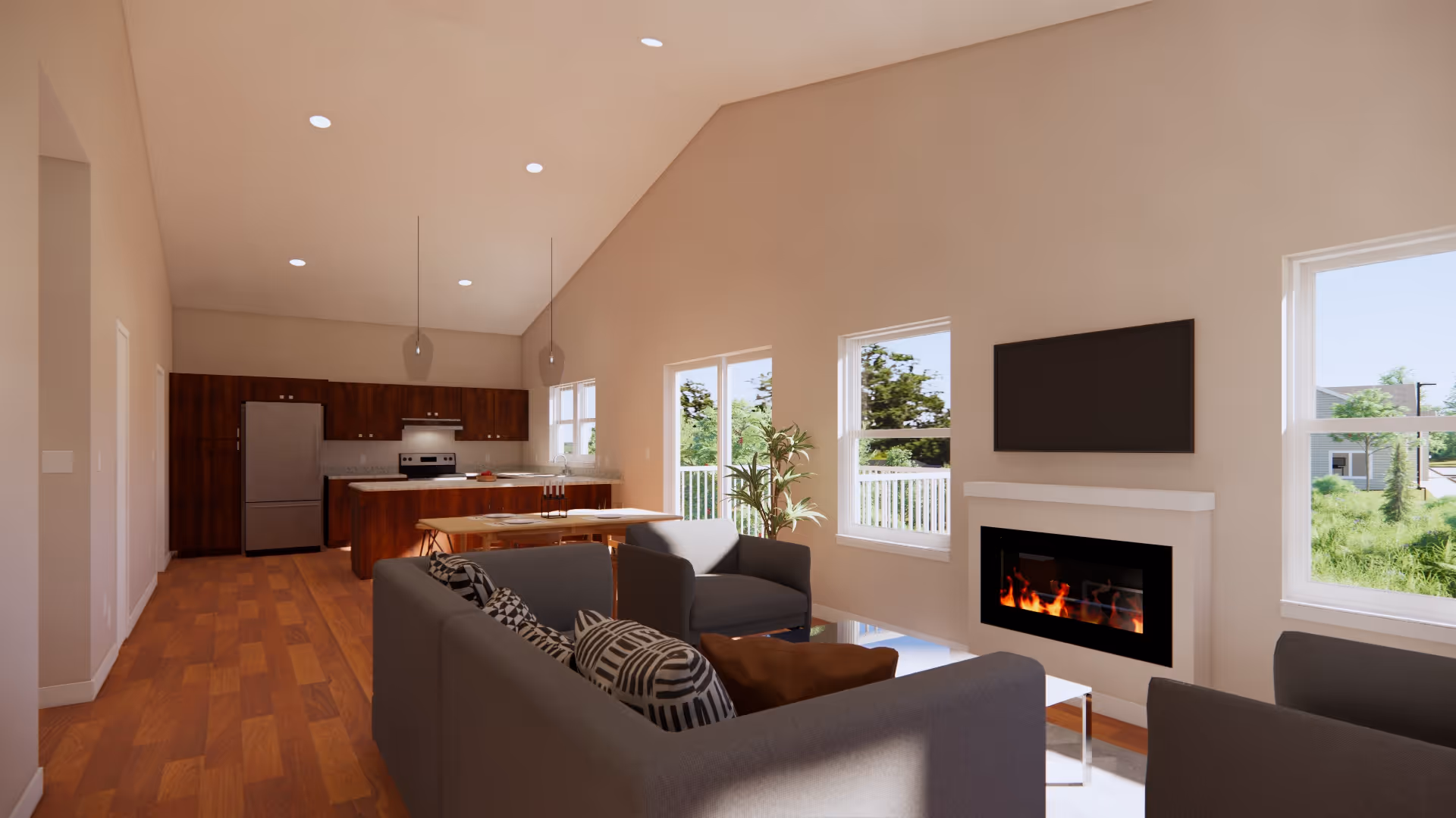 A bright and modern open-concept living room and kitchen area with wooden flooring. The living room features a gray sofa and armchairs with patterned cushions, a white fireplace with a flat-screen TV mounted above it, and large windows letting in natural light. The kitchen has dark wood cabinets, stainless steel appliances, and a dining table with chairs. Pendant lights hang from the ceiling.