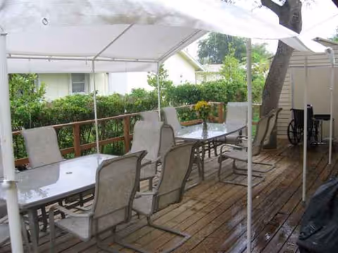 Outdoor wooden deck dining area with tables, chairs, and a canopy at a senior facility.