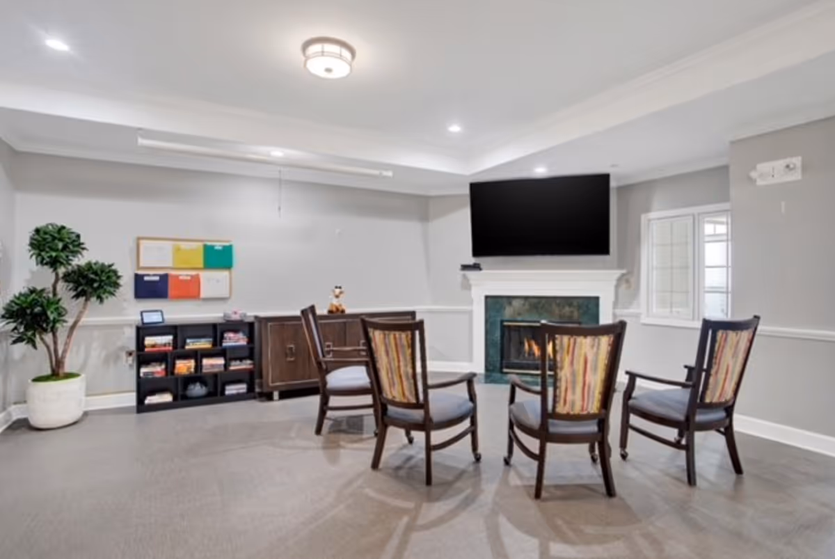 Seating area with four chairs arranged around a fireplace and wall-mounted TV in a bright common room