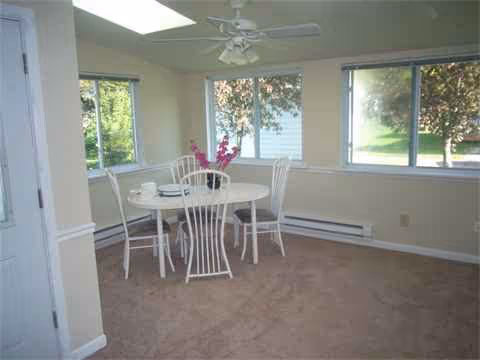 Bright dining area with a round white table, white chairs, and large windows.