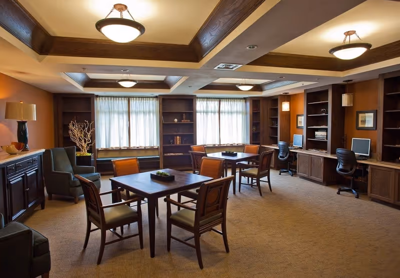 Well-lit communal lounge with tables and chairs, bookshelves, and computer workstations.