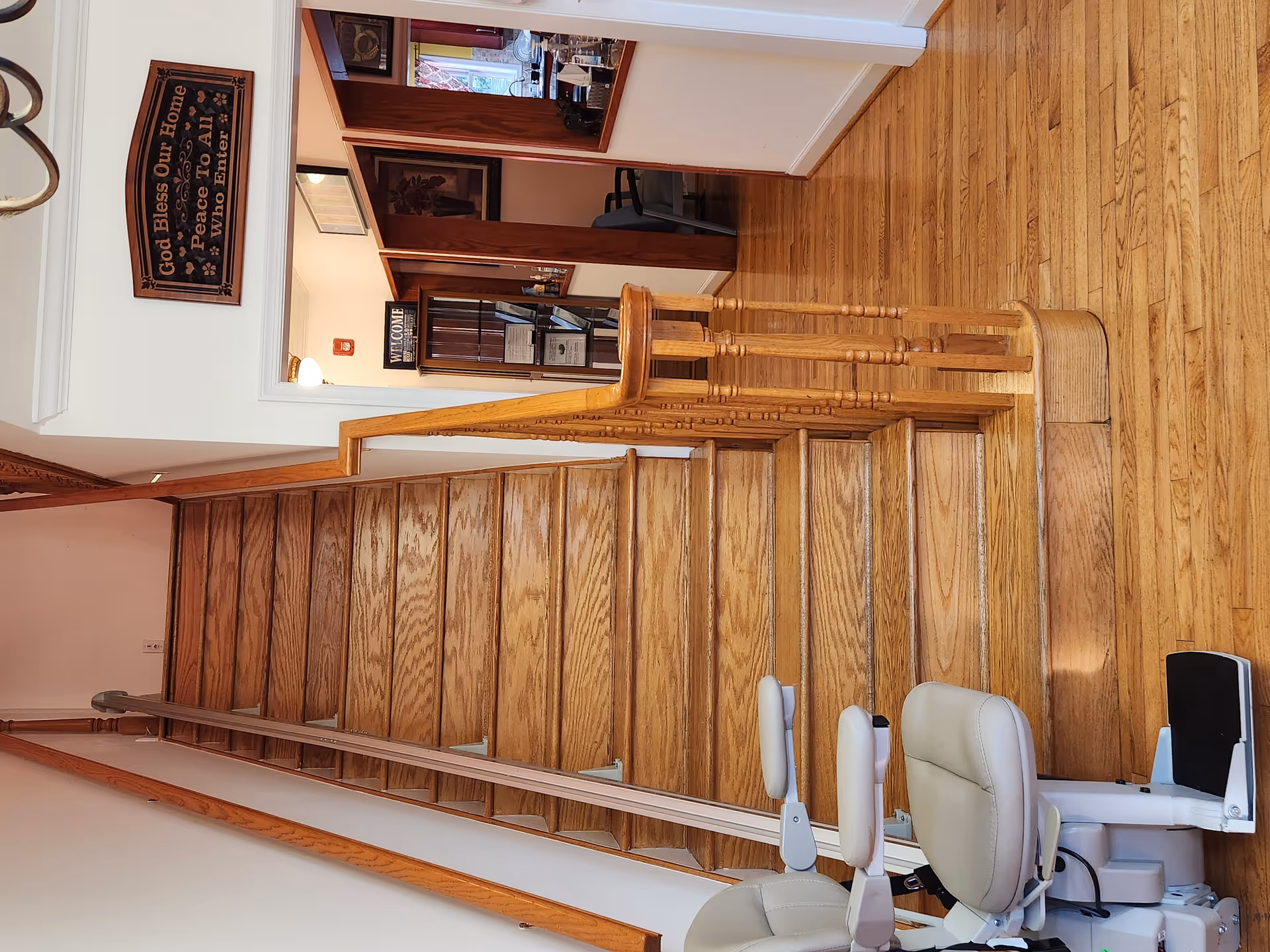 Indoor wood staircase with a beige stairlift chair along the rail, walls and signs visible