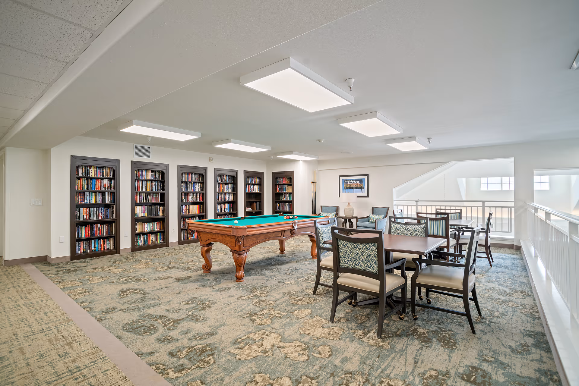 Spacious activity room with a pool table, a wall of bookshelves, and several tables and chairs.