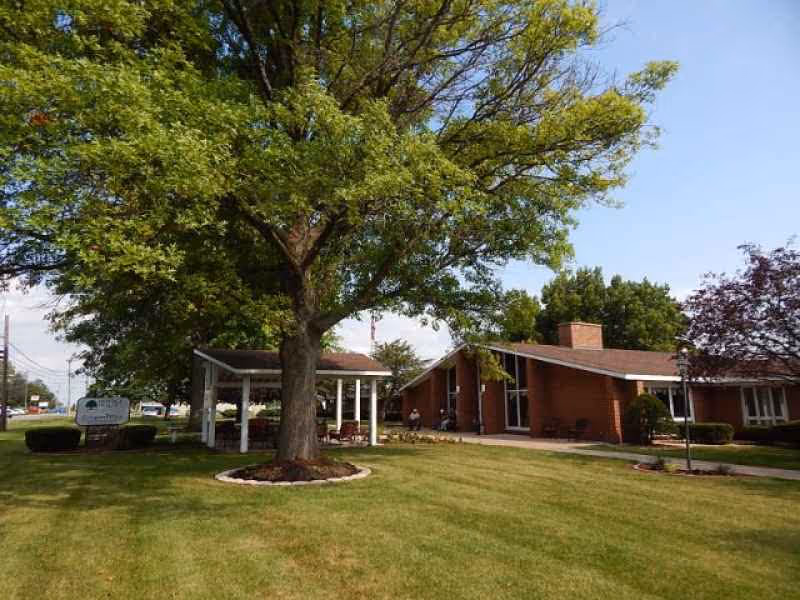 Single-story brick building with a covered entrance, large tree in front, and a manicured lawn.